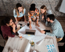 Group of modern business people in casual wear discussing architectural designs in the creative office.