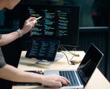 Asian male programmer using stylus to analyze code on tablet and monitor. Software development, coding, and tech workspace concept with real people.